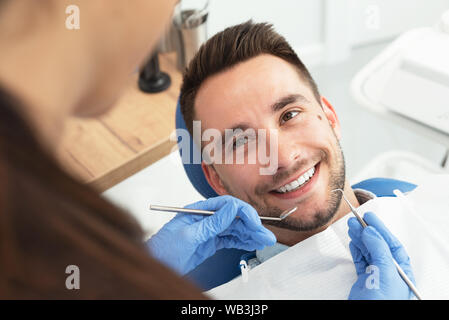 L'homme ayant une visite chez le dentiste. Beau patient assis sur une chaise au bureau de dentiste en clinique dentaire. Banque D'Images