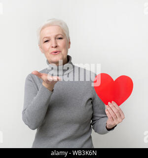 Belle senior woman holding papier rouge coeur et en soufflant des baisers Banque D'Images