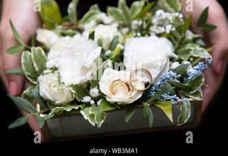 Femme tenant les anneaux de mariage en mains sur les roses blanches bouquet Banque D'Images