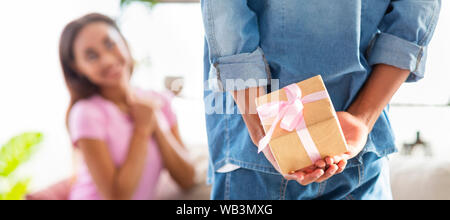 Guy holding présents derrière son dos, surpris fille sur l'arrière-plan. Banque D'Images