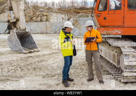 Un homme et une femme ou travailleurs géologues dans casques discuter de quelque chose dans le contexte de l'équipement de construction dans une carrière Banque D'Images