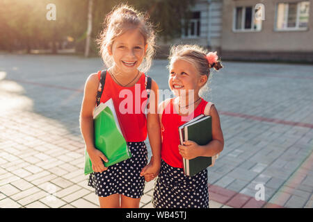 Heureux soeurs filles portant des sacs à dos et la tenue de livres. Kids holding hands outdoors élèves École primaire. L'éducation. Retour à l'école Banque D'Images