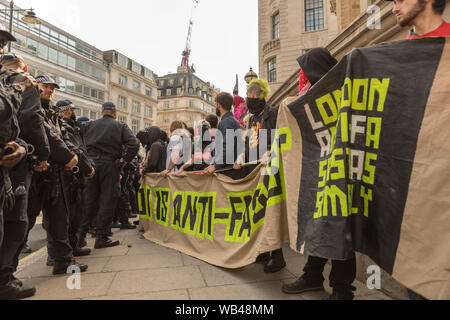 Portland place, Londres, Royaume-Uni. 24 août 2019. Des manifestants portant des banderoles affrontent des policiers lors d'une manifestation antifasciste à Londres. Le texte vert fluo sur les bannières indique « VERS LES ANTIFASCISTES » et « LONDRES ANTIFA DIT FAMILLE ». La toile de fond urbaine comprend des bâtiments et une grue de construction. Gratuit Tommy Robinson proteste devant la BBC. En même temps, une contre-manifestation est organisée par Stand Up to Racism et Unite Against fascism. Penelope Barritt/Alamy Live News Banque D'Images