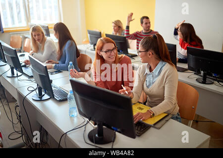 Group of smiling students sitting ensemble à table à l'aide d'ordinateur en classe à l'université. Banque D'Images