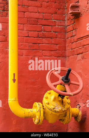 Pipeline de gaz industriels jaune avec le coude et la vanne d'isolation avec poignée rotative, dans le contexte d'un mur de brique rouge Banque D'Images