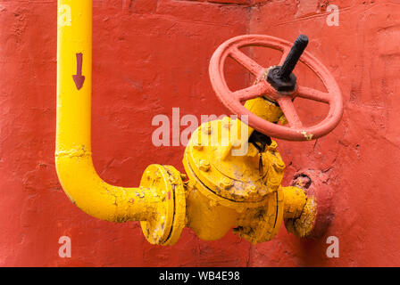 Pipeline de gaz industriels jaune avec le coude et la vanne d'isolation avec poignée rotative, dans le contexte d'un mur de brique rouge Banque D'Images