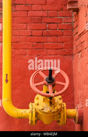 Pipeline de gaz industriels jaune avec le coude et la vanne d'isolation avec poignée rotative, dans le contexte d'un mur de brique rouge Banque D'Images