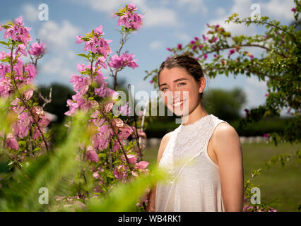 Young caucasian woman est debout à côté de l'usine de bougainvilliers est souriant à l'appareil photo avec des plantes et du ciel en arrière-plan Banque D'Images