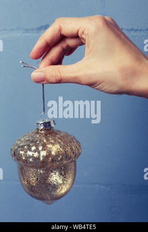 Acorn verre décoration de Noël dans la main contre le mur de couleurs vives. Vacances décoration d'arbre de Noël Banque D'Images