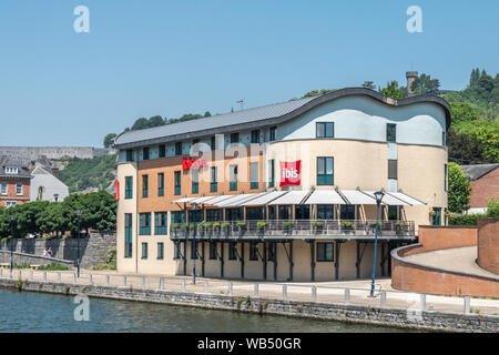 Dinant, Belgique - 26 juin 2019 : Beige et Rouge immeuble pierre de l'hôtel Ibis le long de Meuse soutenu par le feuillage vert. Banque D'Images