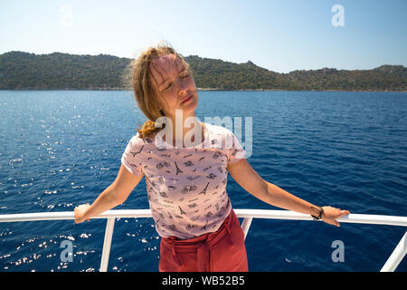 Belle et jeune fille sur un yacht. Une jeune fille se tient avec ses yeux fermé du soleil clair. Derrière le dos de la jeune fille est une mer limpide. Banque D'Images