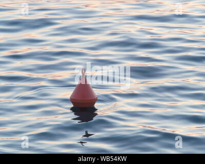 Bouée en plastique orange flottant dans les eaux sombres de l'océan calme au coucher du soleil. La lumière du soleil crée l'ombre et la lumière dans l'eau Banque D'Images