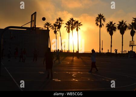 Silhouette de personnes jouant au basket-ball sur un terrain de basket-ball près des cocotiers au coucher du soleil Banque D'Images