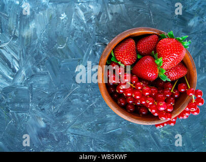 Bol de fruits des rouges sur fond gris. Mélange de petits fruits. Delicious fresh ripe de groseille rouge et de fraise dans un bol marron, plaque, lave. Berry isolés Banque D'Images
