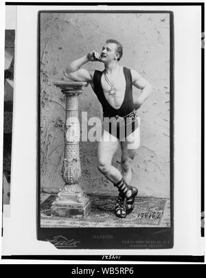 Eugene Sandow, portrait en pied, debout, appuyé sur la colonne, orienté vers la gauche, le port de collants, de lutte, et Romain sandles pendentif étoile à six pointes Abstract/moyenne : 1 tirage photographique. Banque D'Images