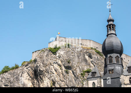 Dinant, Belgique - 26 juin 2019 : Libre de Citadelle avant haut avec pavillon belge et flèche de l'église Notre-Dame sur fond de ciel bleu. Banque D'Images