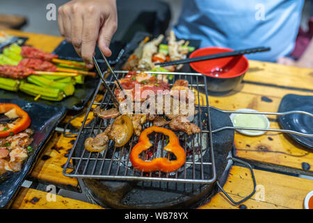 Man grilling tranches de viande et poivrons sur un charbon cuisinière Banque D'Images