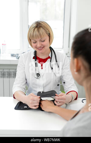 Femme médecin professionnel mise sur l'appareil de mesure de pression sur les jeunes patients de sexe féminin dans la chambre d'hôpital. Banque D'Images