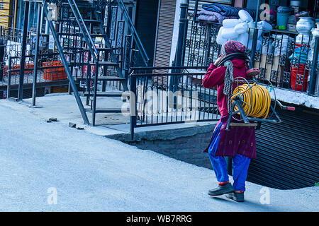 Shimla, Himachal Pradesh, Inde - Juillet 20th, 2019 : Indian Women walking on street.de soulever des poids lourds rouleaux de câble électrique sur sa tête. Banque D'Images