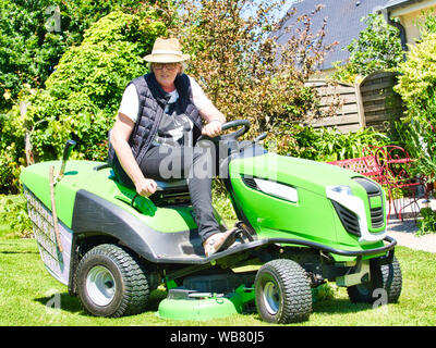 Woman hat conduisant un tracteur tondeuse de jardin avec fleurs. En vert et blanc sur la faucheuse, virage dans le champ entre fleurs colorées. C Banque D'Images