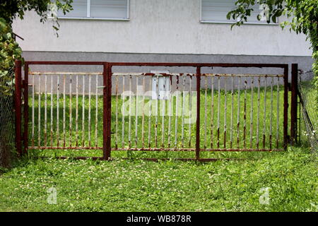 Complètement blanc rouillé vieux clôture métallique avec portes fermées et boîte aux lettres monté entouré d'herbe non coupée et d'autres plantes de jour d'été chaud et ensoleillé Banque D'Images