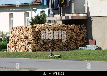 Bois de chauffage empilé fraîchement préparé pour les jours froids de l'hiver en face de la maison de famille balcon entouré d'herbe et des routes pavées sur jour d'été chaud et ensoleillé Banque D'Images