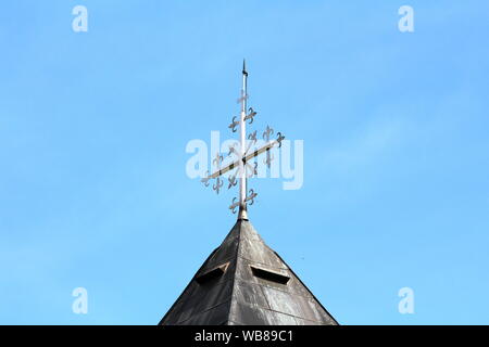 Vue latérale du haut de toit de l'église locales du pays couvert de tuiles vieux métal métal brillant et inhabituelle, une croix sur fond de ciel bleu clair Banque D'Images