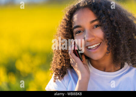 Portrait plein air de beautiful happy mixed race biracial African American girl adolescent femme jeune femme avec dents parfaite talking on cell phone Banque D'Images