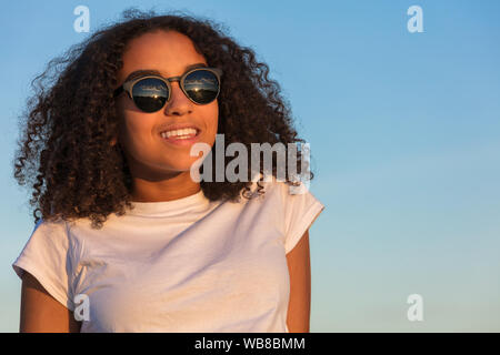 Mixed Race girl biracial adolescent femme jeune femme parfaite avec les dents au coucher et au lever du soleil le port de lunettes de soleil Banque D'Images