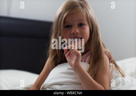 Fille 6 ans montre la dent de lait tremblotantes assis sur le lit après le sommeil Banque D'Images