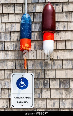 Seul signe de stationnement pour personnes handicapées sur un mur dans le Maine avec des bouées de homard suspendues au-dessus de lui. Banque D'Images