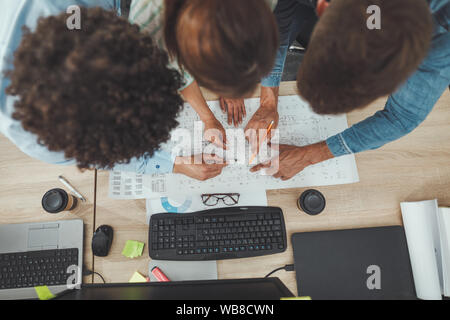 Équipe de trois jeunes architectes travaillent sur un nouveau projet et la communication pendant l'analyse de plans dans le bureau. Vue d'en haut. Banque D'Images