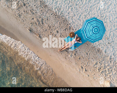 Vue de dessus d'une belle jeune femme qui connaît dans le soleil sur la plage vêtue d'un bikini. Elle est en train de vous détendre sur la plage bleue serviette sous le bl Banque D'Images