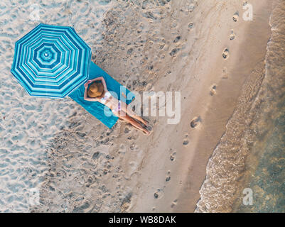 Vue de dessus d'une belle jeune femme qui connaît dans le soleil sur la plage vêtue d'un bikini. Elle est en train de vous détendre sur la plage bleue serviette sous le bl Banque D'Images