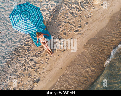 Vue de dessus d'une belle jeune femme qui connaît dans le soleil sur la plage vêtue d'un bikini. Elle est en train de vous détendre sur la plage bleue serviette sous le bl Banque D'Images