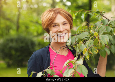 Femme mature en bonne santé s'amusant avec des feuilles vertes à l'extérieur. Beau modèle 60 ans Banque D'Images