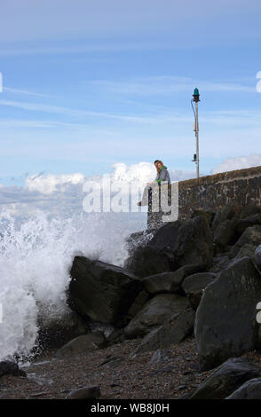 Un couple s'asseoir sur la digue du port du bras à Lynmouth avec mer agitée vagues se brisant sur les rochers au-dessous Banque D'Images