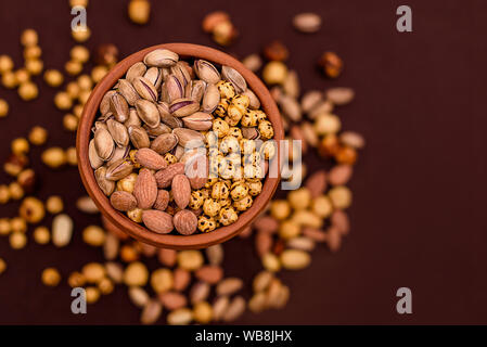 Amandes, pistaches, noisettes et les noix dans un bol rond texturé sur fond brun. Le tableau Vue de dessus de la nourriture. Banque D'Images