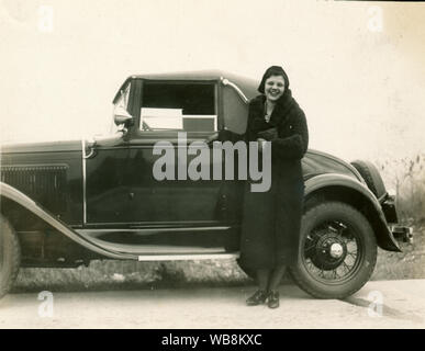 Photographie jaunie de 1933 d'une jeune femme avec un Ford Model A Sport coupé d'environ 1928-1932. Banque D'Images