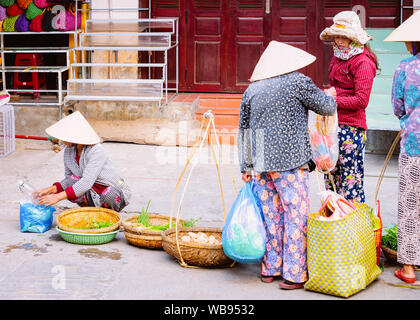 Hanoi, Vietnam - 17 Février 2016 : Les femmes marchands de chapeaux vietnamiens traditionnels vendre et acheter de la nourriture sur la rue du marché à Hoi An au Vietnam en Asie. Les petites entreprises locales avec les vendeurs et fournisseurs Banque D'Images