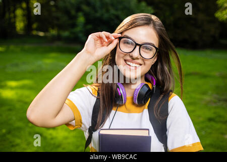 Portrait of cheerful student girl lunettes de réglage sur un campus park lawn Banque D'Images