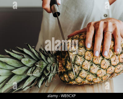 Femme blonde aux yeux verts dans la cuisine moderne et sur le point de préparer un ananas. Banque D'Images