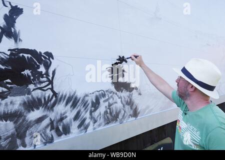 L'artiste britannique David Downes a été commandé par ITV pour créer une grande murale public à Bournemouth en avance sur le lancement de leur drame 2019 Sanditon en août 2019. Peinture publiquement pour 5 jours, Downes recréera une version illustrée de l'art de l'affiche pour un géant sur Sanditon, Billboard dans la ville côtière du Royaume-Uni, pour tenir compte de l'environnement du bord du drame. L'installation restera en place pendant trois semaines après son achèvement. David Downes est un peintre de paysages qui amplifie le sens du lieu et l'heure à travers l'objectif de l'autisme. Banque D'Images