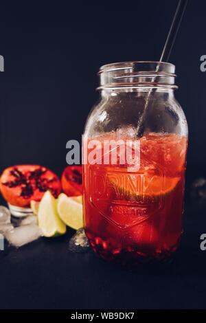 cliché vertical d'un bol en verre rempli de grenade pressez avec une paille sur fond noir Banque D'Images