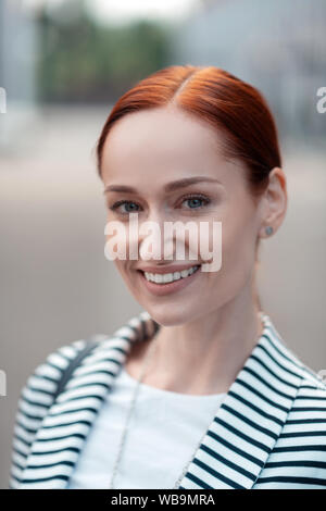 Smiling beautiful blue-eyed red-haired young woman standing outdoors Banque D'Images