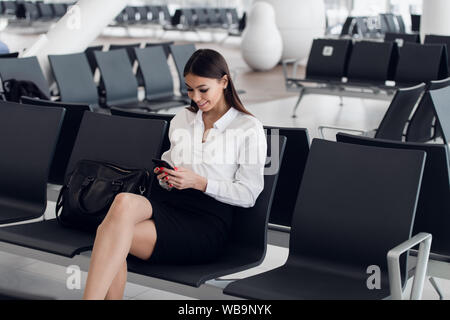 Woman Reading Messages téléphoniques en salle d'attente de l'aéroport. Happy girl acheter e-ticket, faire des réservations d'hôtel et de l'enregistrement en ligne Banque D'Images