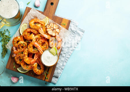 Brochettes de crevettes grillées ou langoustines servies avec de la chaux, de l'ail et de la sauce sur fond de béton bleu clair. Fruits de mer et bière. Vue de dessus avec copie Banque D'Images