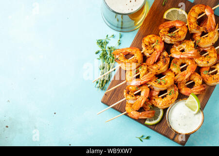 Brochettes de crevettes grillées ou langoustines servies avec de la chaux, de l'ail et de la sauce sur fond de béton bleu clair. Fruits de mer et bière. Vue de dessus avec copie Banque D'Images