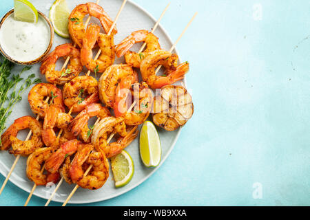 Brochettes de crevettes grillées ou langoustines servies avec de la chaux, de l'ail et de la sauce sur fond de béton bleu clair. Fruits de mer et bière. Vue de dessus avec copie Banque D'Images