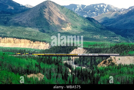 Locomotives diesel 1 Place de l'état de l'Alaska Railroad tirez sur les bagages et les voitures avec l'observation des passagers à travers les touristes un tréteau qui enjambe une rivière sur le chemin de Denali National Park et de préserver dans l'Alaska, USA. Ce voyage ferroviaire dispose de magnifiques paysages de montagne et la vallée de 356 milles (573 kilomètres) entre Anchorage et Fairbanks. Un point fort est quand le train passe au mont McKinley (Denali), également appelé le plus haut sommet de montagne en Amérique du Nord à 20 237 pieds (6 168 mètres). Banque D'Images
